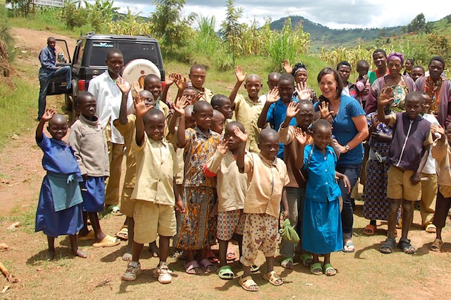 Examining the Challenges, Future, & Benefits of Fair Trade Group of school aged african children standing and waving with a representative from Fair Trade Certified - Cait Bagby