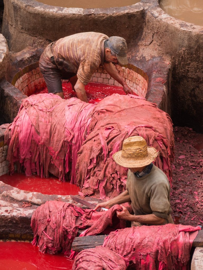 10 Million Enslaved in Bondage Labor Worldwide - Photo of two men working outside in a traditional textile dyeing factory. They are using the color red - Cait Bagby