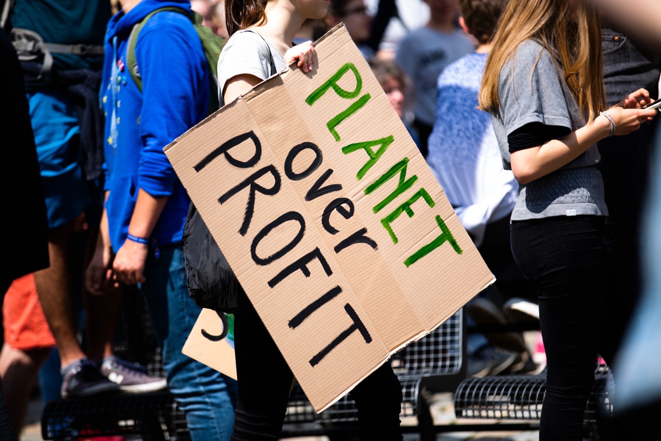 Breaking Down the ESG Umbrella with Economist Rocco Ciciretti - Photo of a climate change protestor holding a cardboard sign with the world Planet over Profit written on it - Cait Bagby
