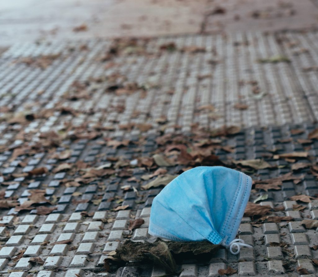 Environmental Impact of PPE - photo of a disposable blue face mask discarded on a city sidewalk - Cait Bagby